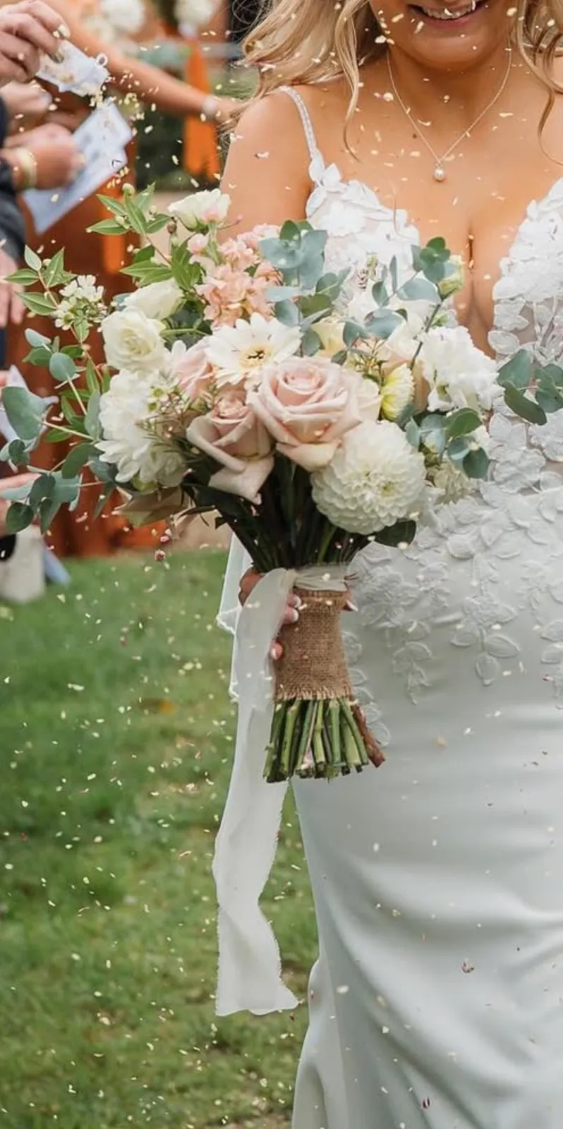 Bride carrying a blush and white bouquet of roses, dahlias and eucalyptus through confetti
